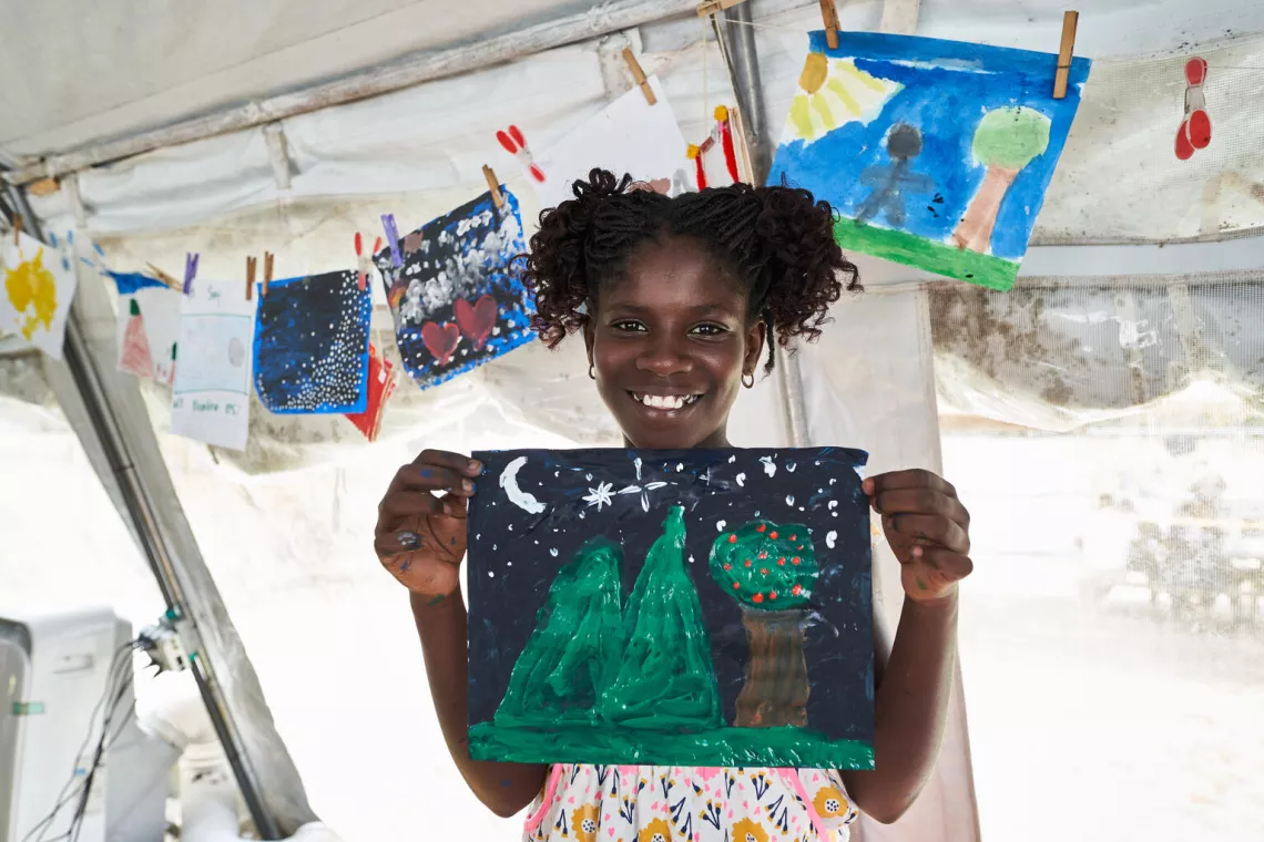 A migrant girls shows her drawing of mountains.