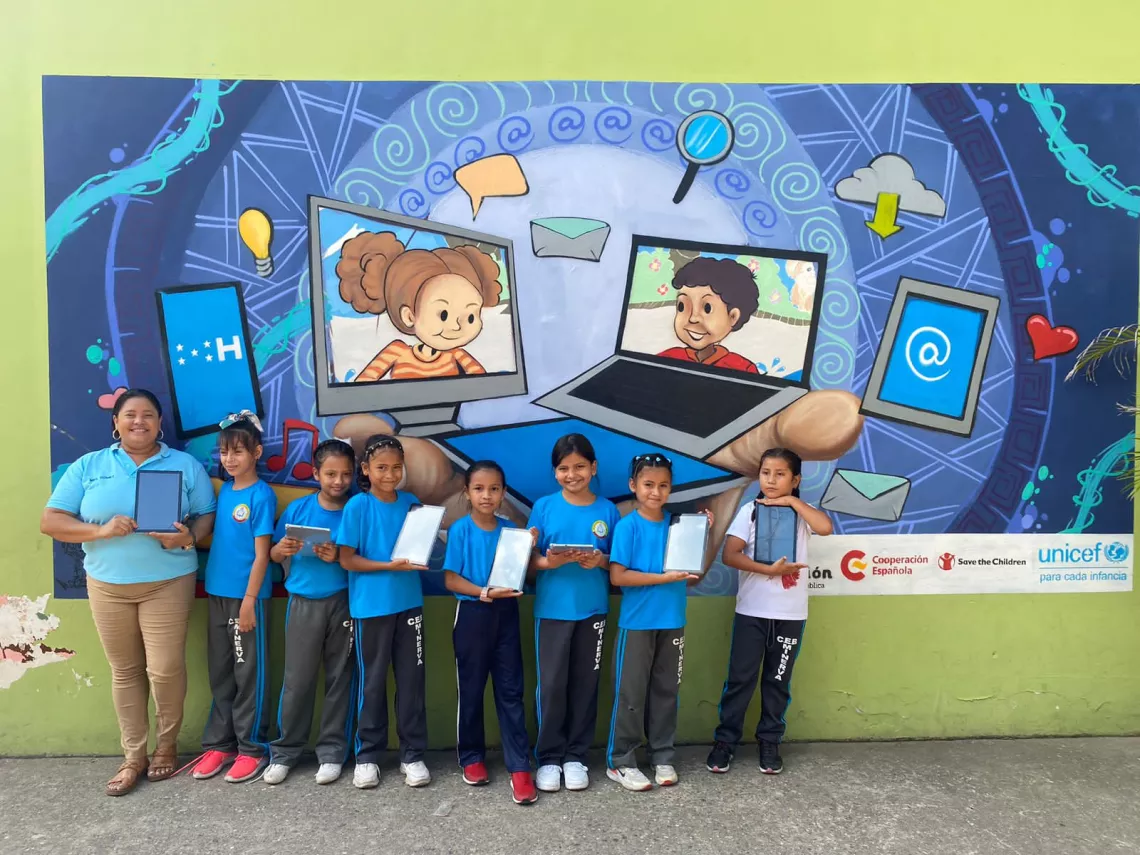 Group of girls with their teacher holding tablets in front of a mural