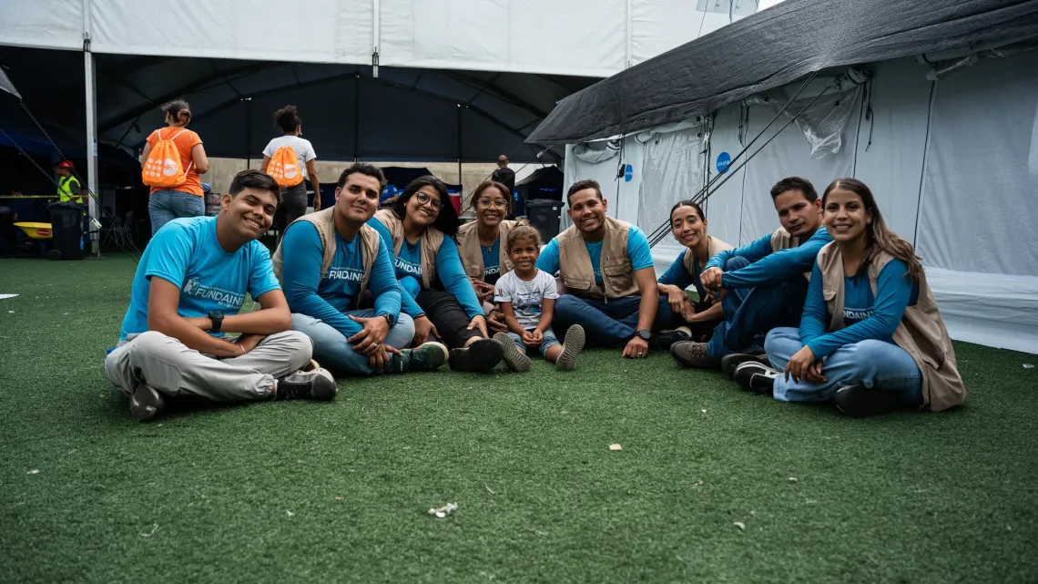 Un grupo de personas, y una ni&ntilde;a al centro, sentadas en semicirculo, frente a una carpa