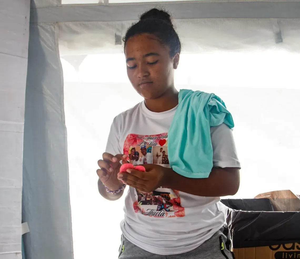 Una adolescente, de pie, dentro de una carpa que forma parte de un campamento transitorio