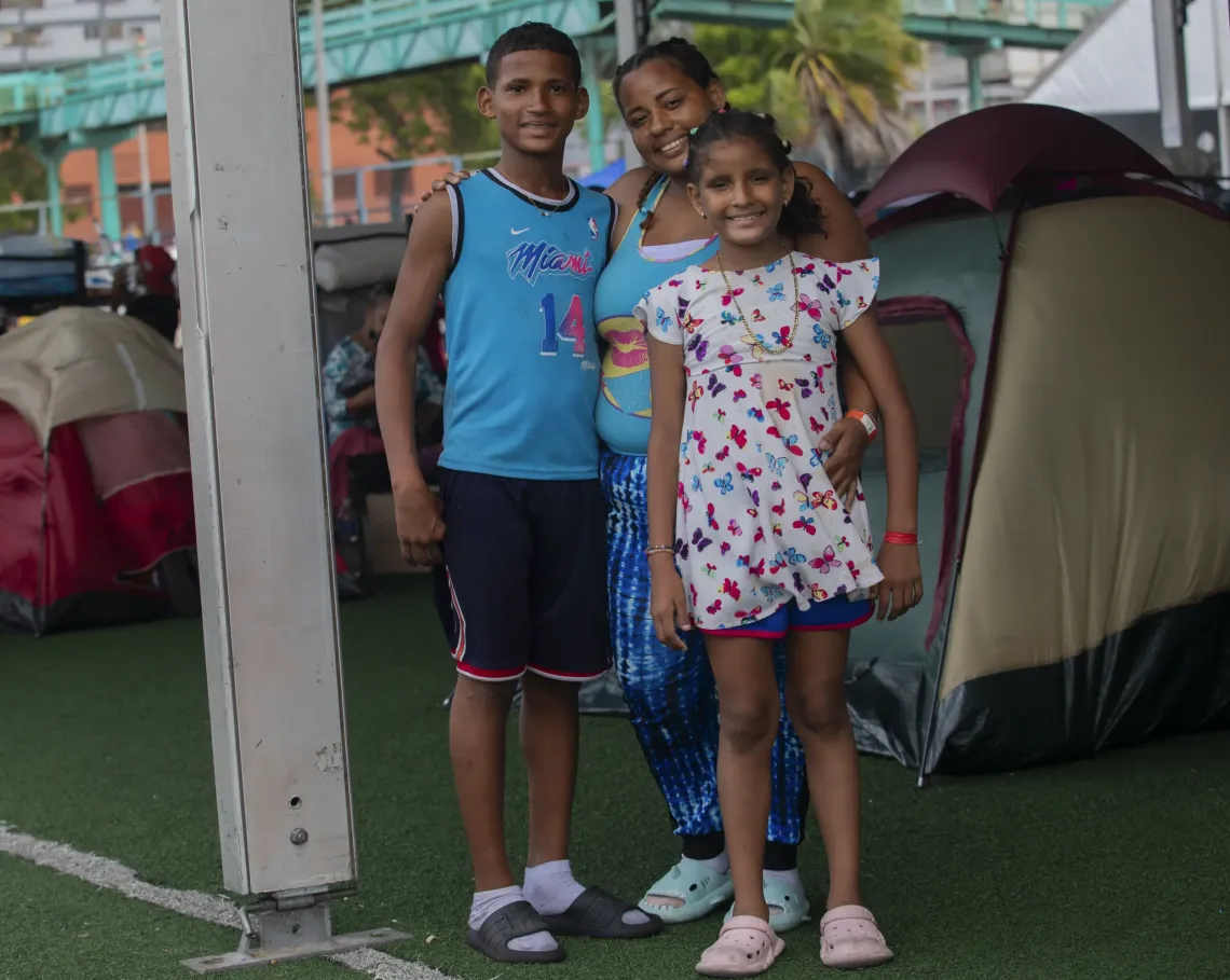 Una mujer de pie, abrazando a un adolescente y una ni&ntilde;a, delante de una carpa, mientras los tres sonr&iacute;en