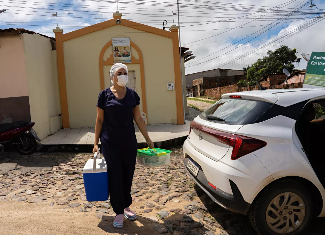 A nurse carrying a cooler box, walks towards a car.