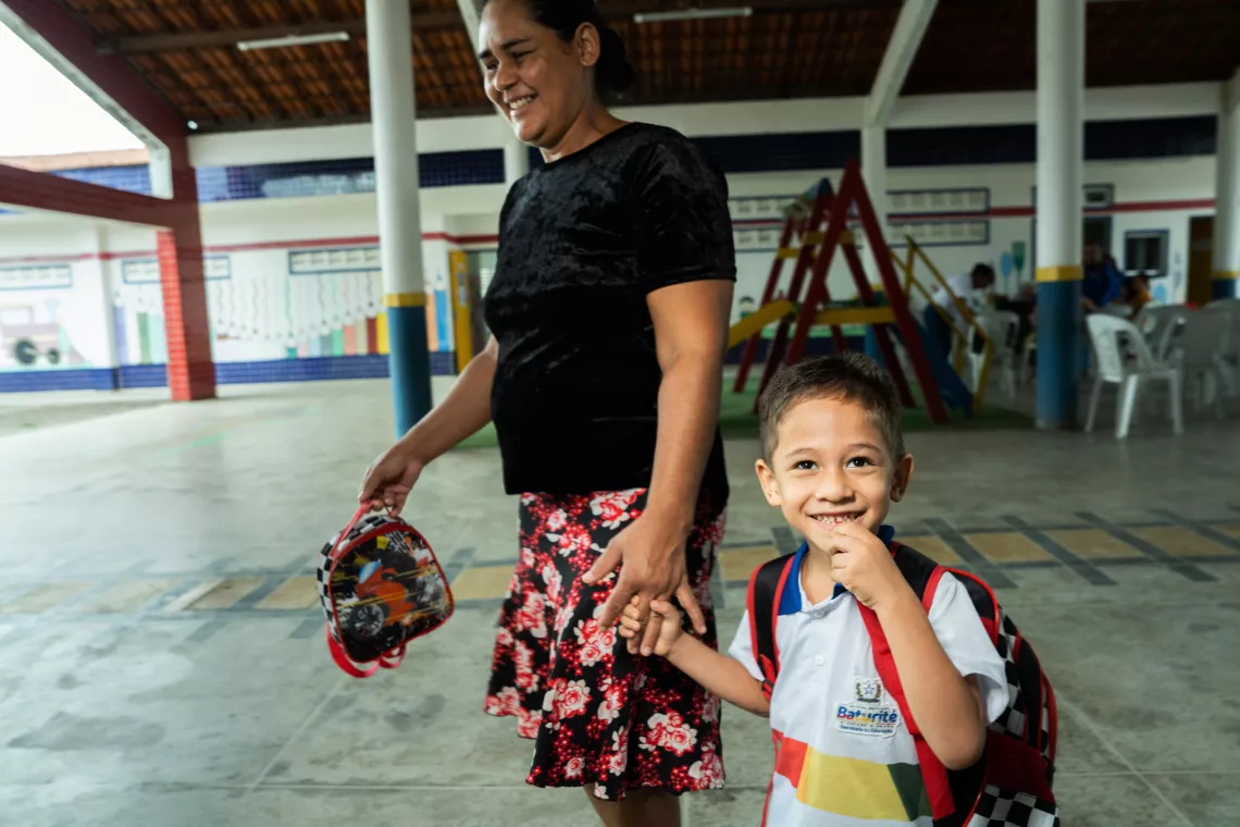 Young boy holding his mother's hand looks up at the camera.
