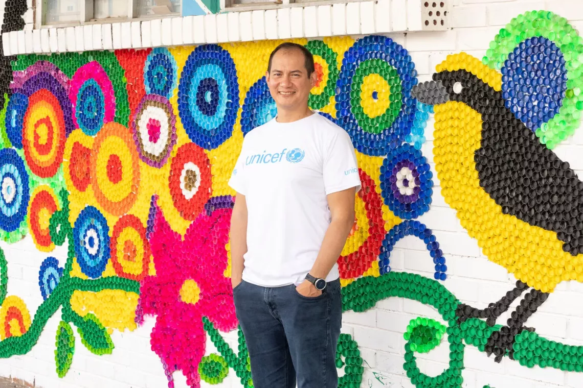 El oficial de Protecci&oacute;n del &Aacute;rea de Migraciones de UNICEF en Colombia posa frente a un mural colorido. 