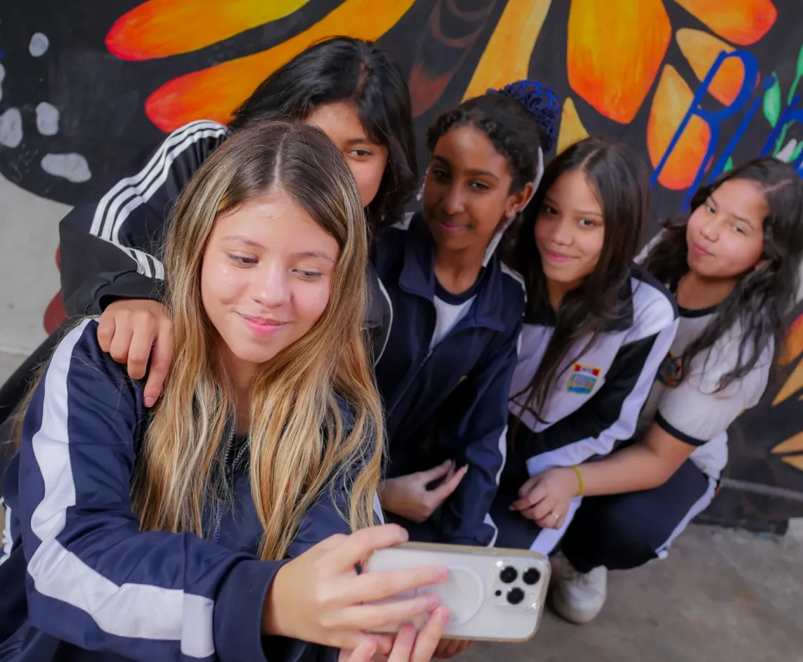 Five teenage girls in school uniform are taking a selfie photo with an Iphone.