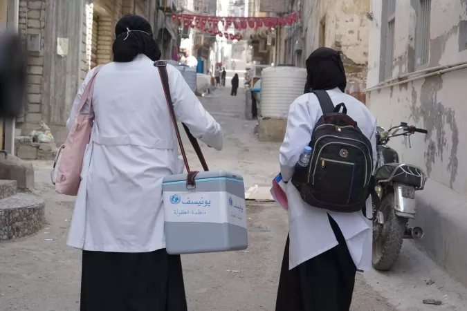 Two healthcare workers care refrigerators full of vaccines.