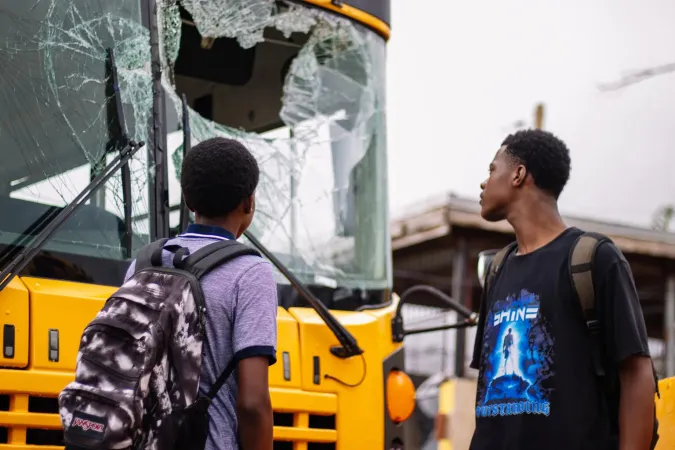 Dos j&oacute;venes ven un autobus escolar destruido por el hurac&aacute;n 