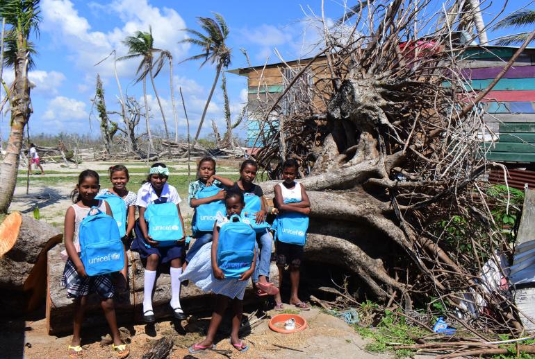 Girls with UNICEF-provided backpacks in front of a large fallen tree.