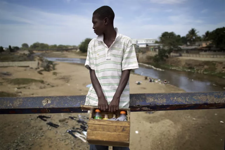 Un ni&ntilde;o con una caja de madera se apoya en la barandilla de un puente en la ciudad de Ouanaminthe, en la frontera noreste con Rep&uacute;blica Dominicana. 