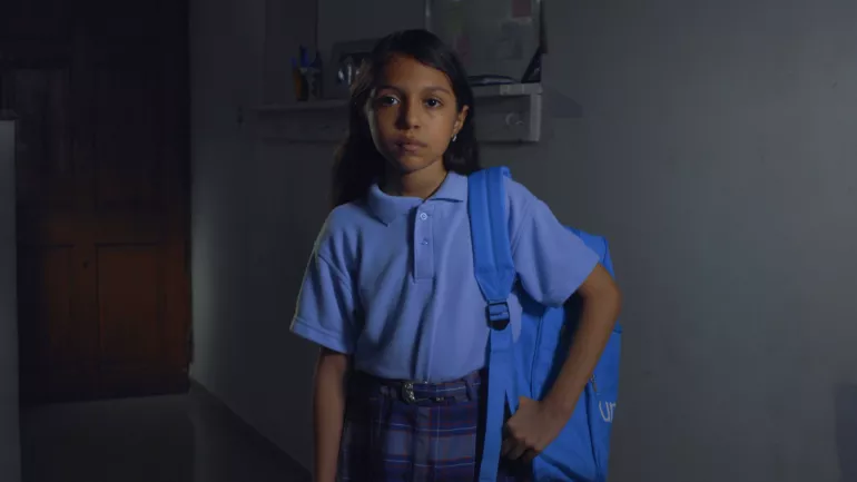 Ni&ntilde;a en uniforme con mochila en un hombro.