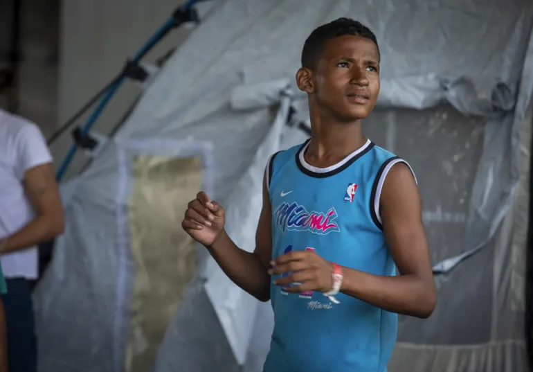 Un adolescente de pie, dentro en un campamento temporal.