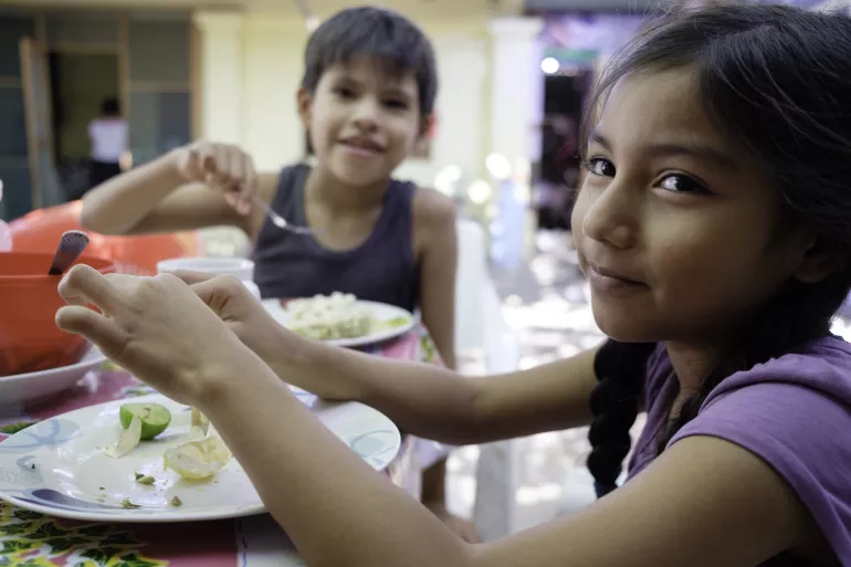 Dos ni&ntilde;os sentados a la mesa de una casa, desayunando