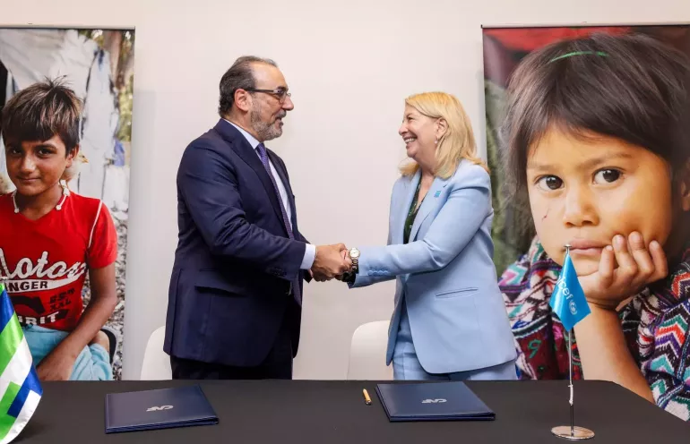 Two persons shaking hands with a background of children photos in the wall