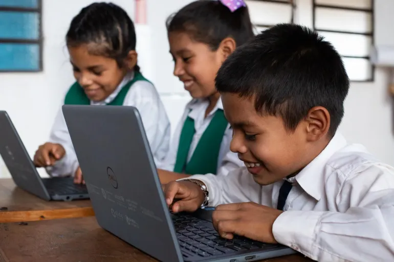 Dos ni&ntilde;as y un ni&ntilde;o con computadoras en un sal&oacute;n de clases 