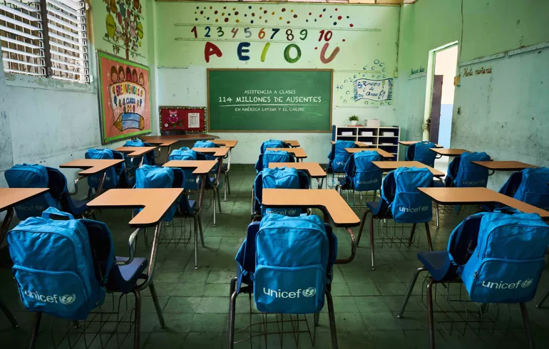 Sal&oacute;n de clases vac&iacute;o con mochilas en el respaldar de las sillas.