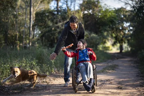 Arturo Javier Rivarola Gimenez, 11, is pushed in his wheelchair by his father, Carlos Andres Rivarola, 46, while waving a toy "light saber" at the family's pet dog in Limpio, Central District, Paraguay on 3 August 2019.