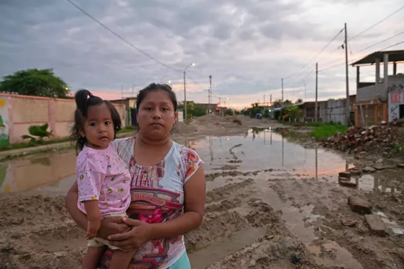 A woman holding her child on a muddy road