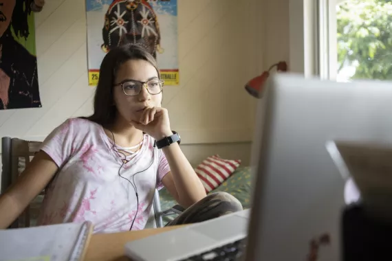 Una j&oacute;ven est&aacute; sentada frente a una computadora tomando una clase de historia 