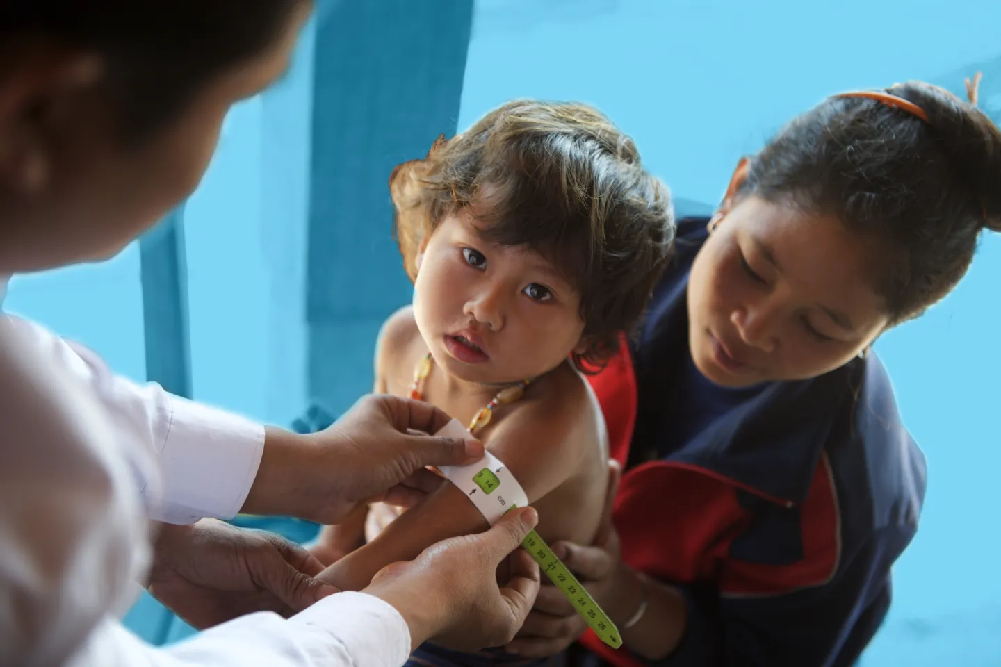 ັA male health worker takes child's measurement of upper arm circumference (MUAC) 