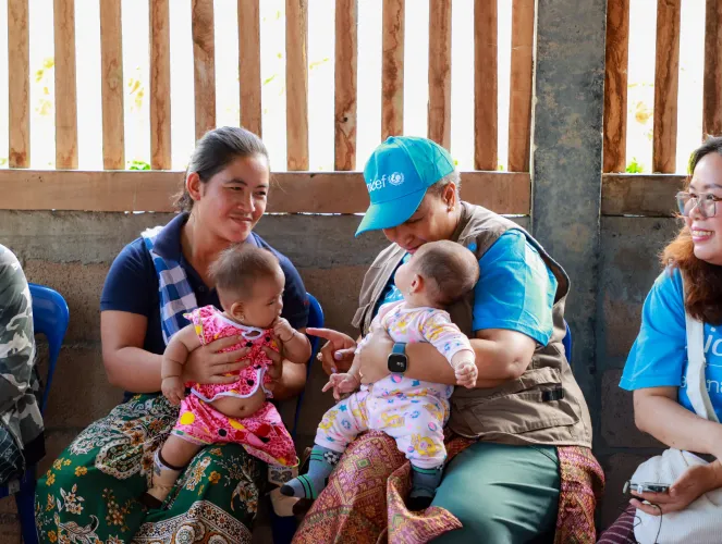 A UNICEF member holds a baby while sitting next to a mother with her infant during a community visit.