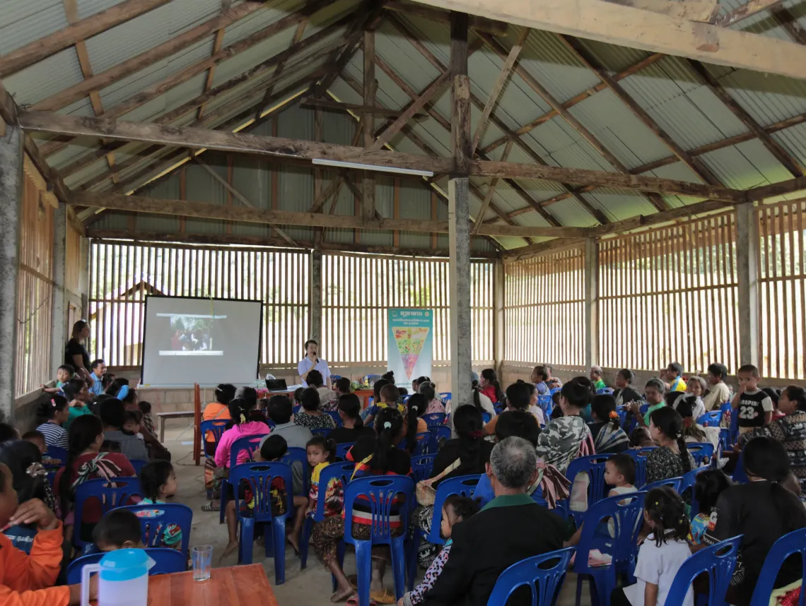 A facilitator presents on child nutrition to parents and community members during a community session in a rural village hall in Lao PDR.
