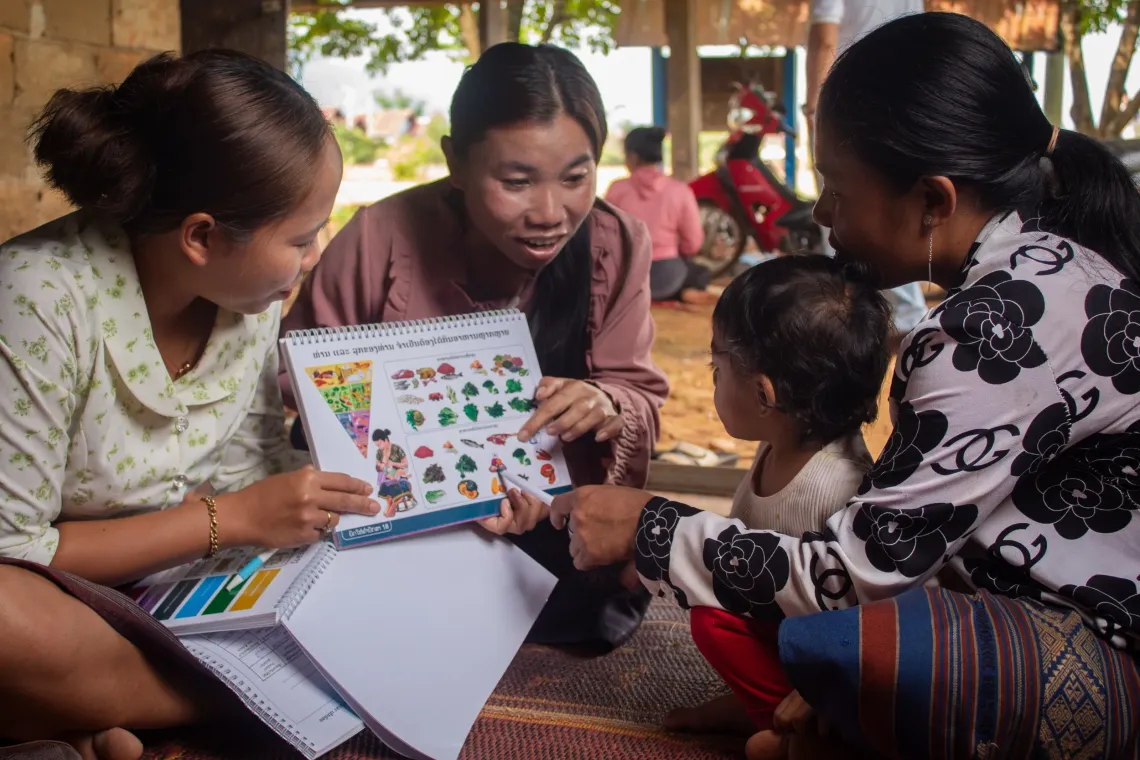 Health workers guide a mother and her young child through a nutrition education booklet during a community parenting session in Lao PDR.
