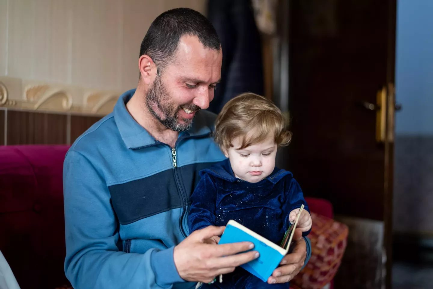 Father of Jinane, 1 year old, holding her and reading a story 