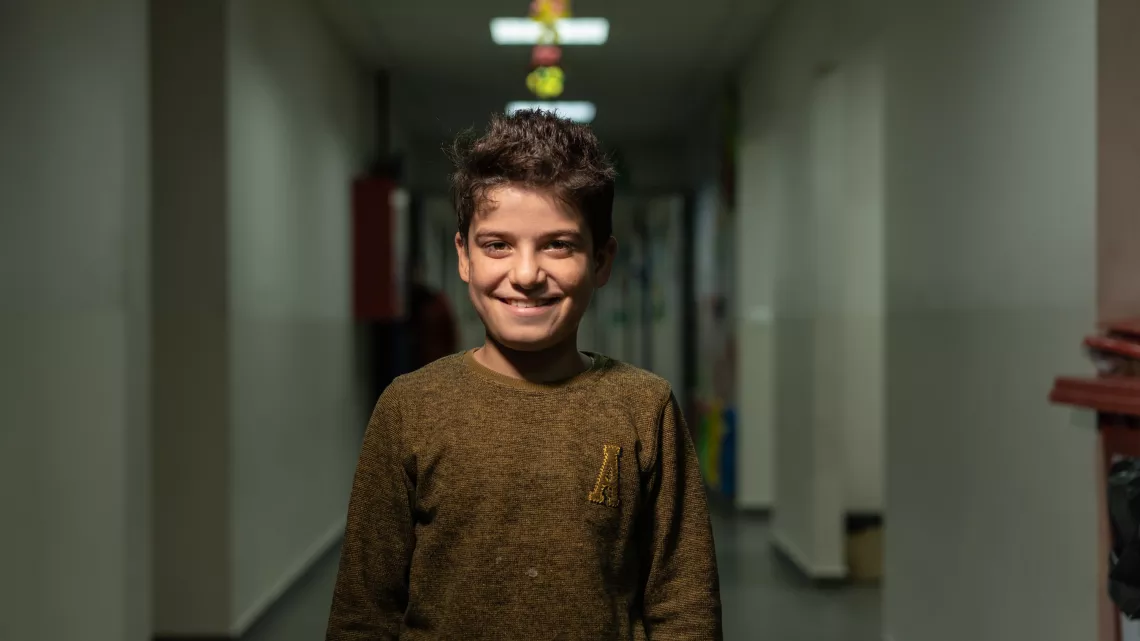 Hayan stands in a school hallways, with a big smile on his face
