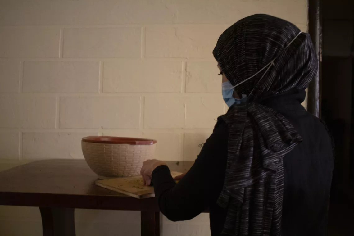 Sara, a 31-year-old mother-of-three sits in an unlit kitchen chopping vegetables 