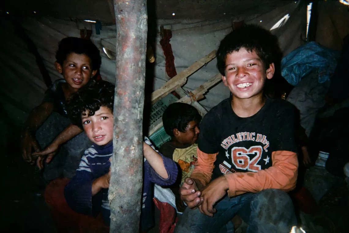 Children sitting inside their makeshift shelter smiling to the camera.
