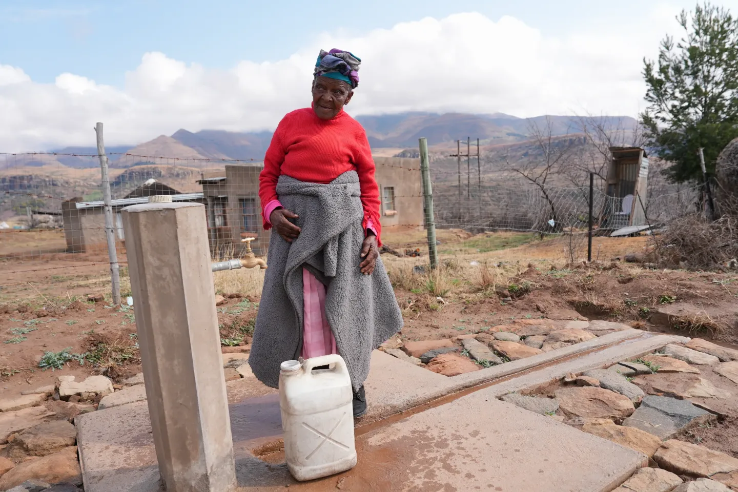 A woman stands before an outdoor water tap