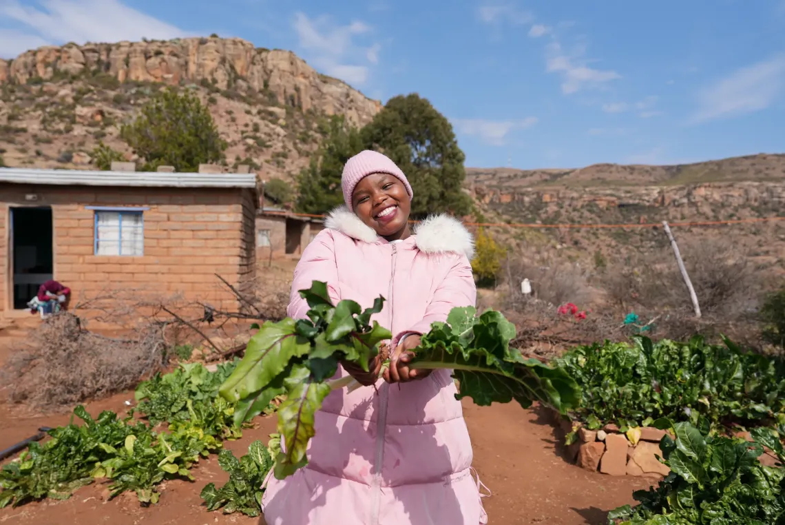 A woman smiles while outside holding fresh greens from a garden
