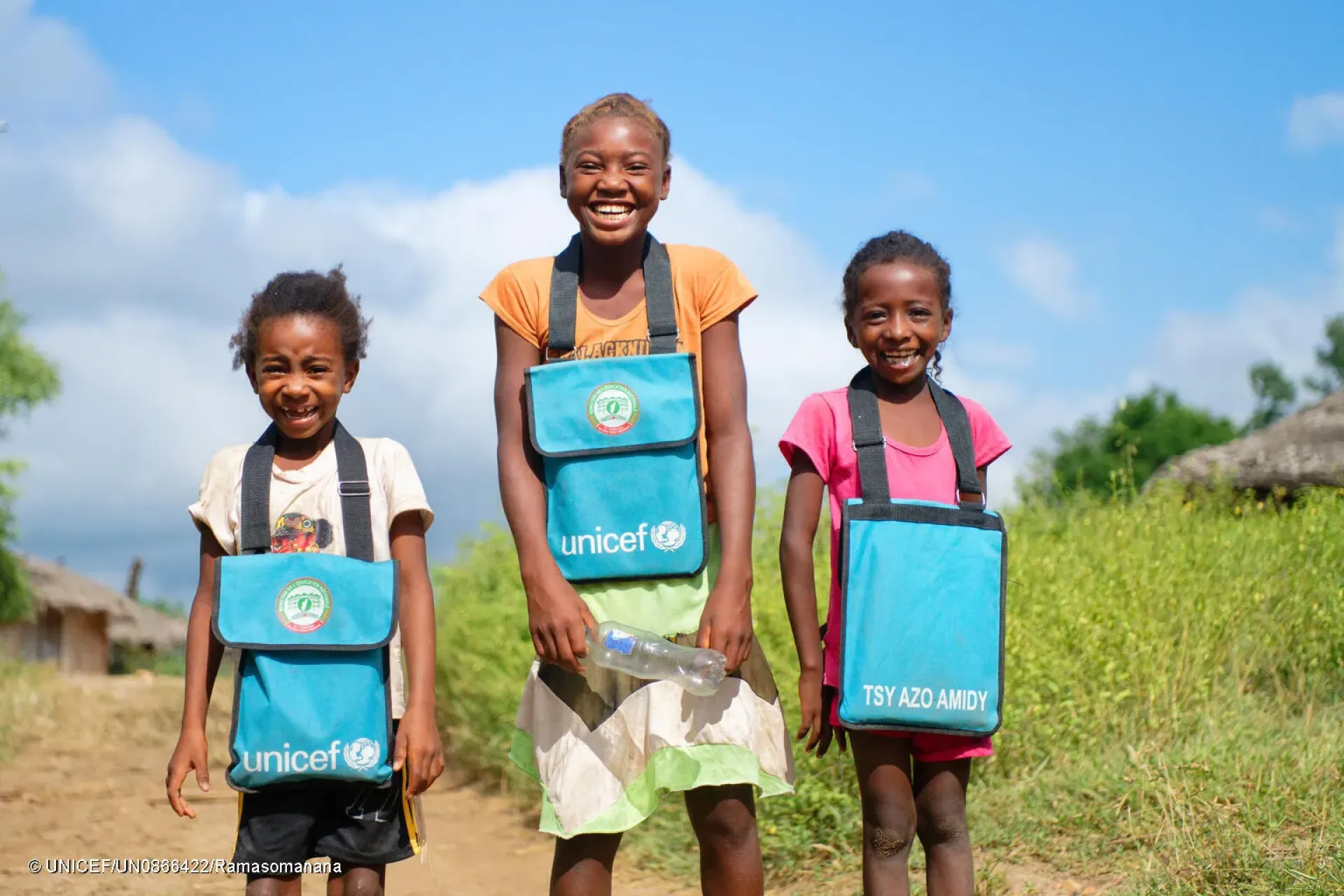 Village d&rsquo;Antanandava, au nord-ouest de Madagascar : photo de groupe de trois &eacute;coli&egrave;res souriantes de l&rsquo;&Eacute;cole primaire publique portant des cartables fournis par l&rsquo;UNICEF.