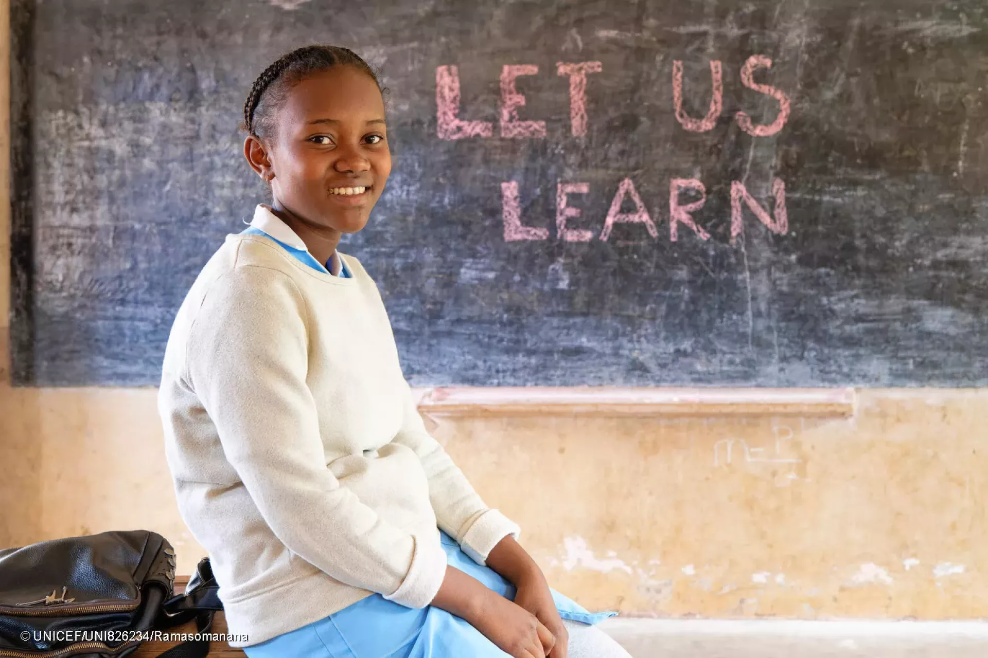 portrait of Aim&eacute;lia taken in front of a blackboard where it is written "Let Us Learn".