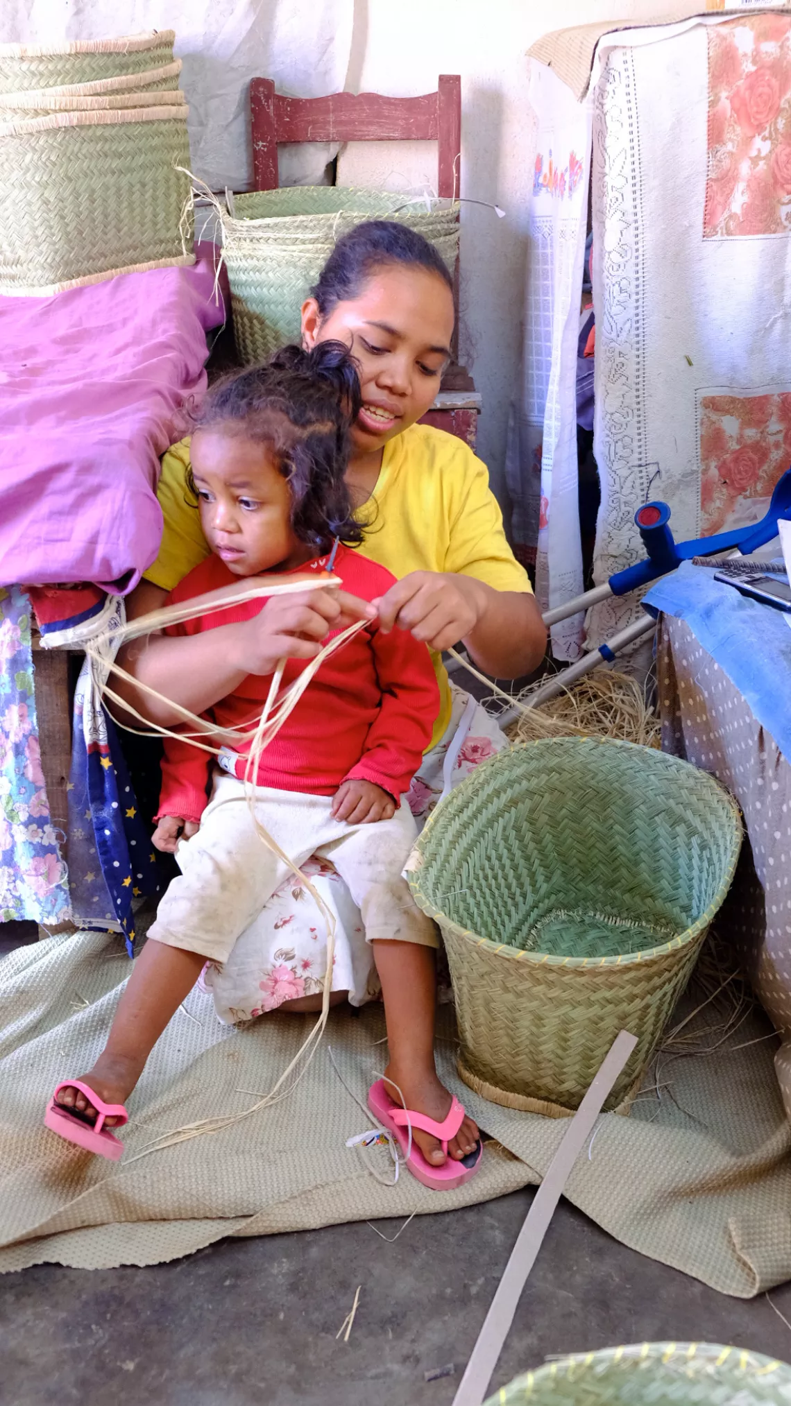 Une maman, avec son enfant sur les genoux, tresse de la natte pour en faire un panier
