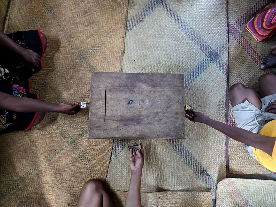 Ambonaivo village, Vavatenina District, Analanjirofo Region, Madagascar: Three members of the community savings group opening the box containing the collective fund and administrative documents before the meeting begins.