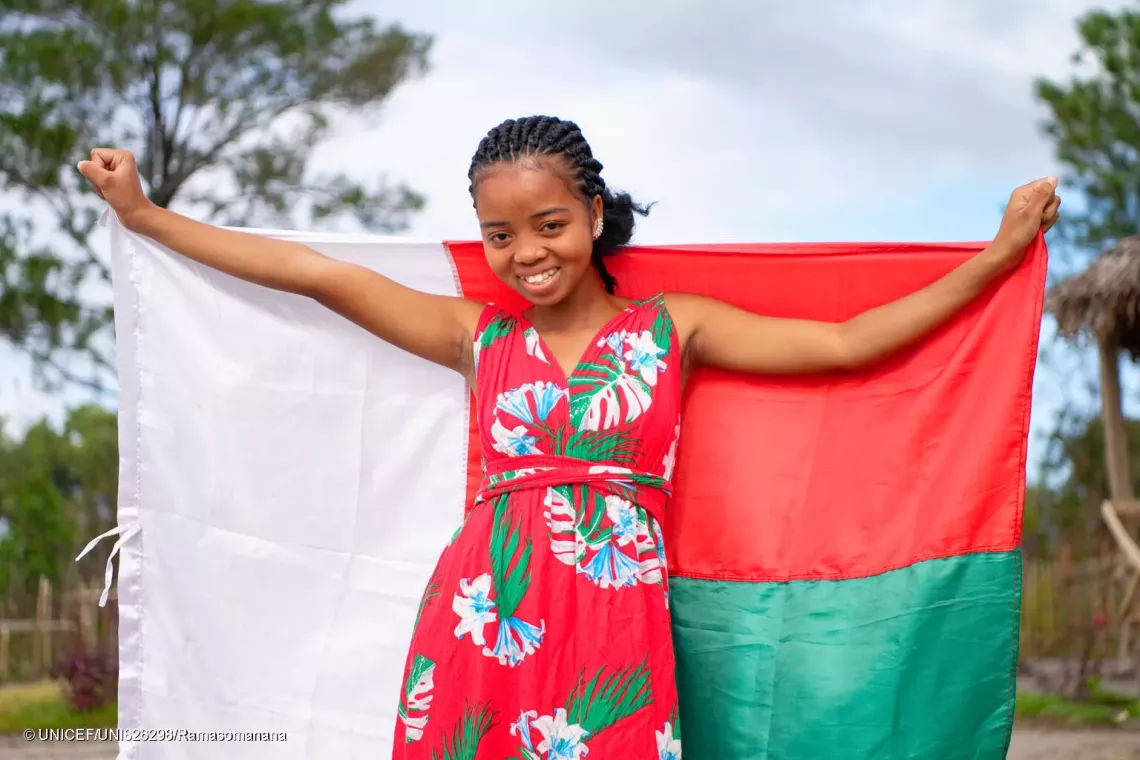portrait of Yolande, 14, holding the Malagasy national flag before the start of a listening group with around thirty children and adolescents