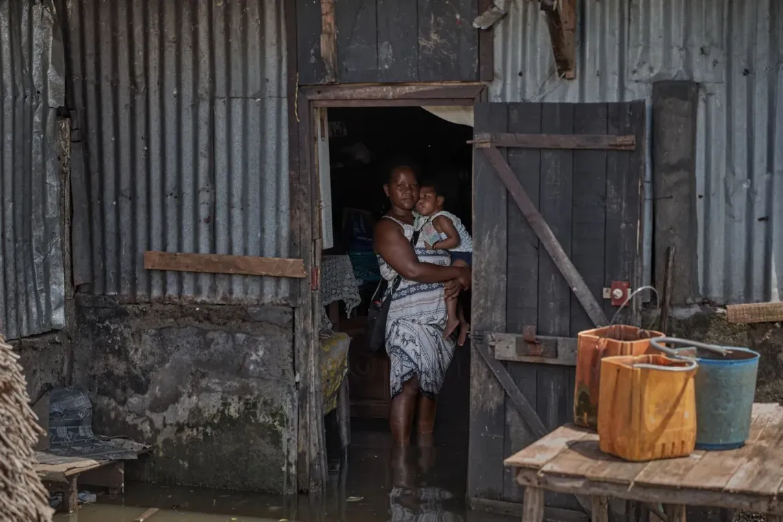 Jacqueline and her baby on the doorstep of their home damaged by Cyclone Gezani.