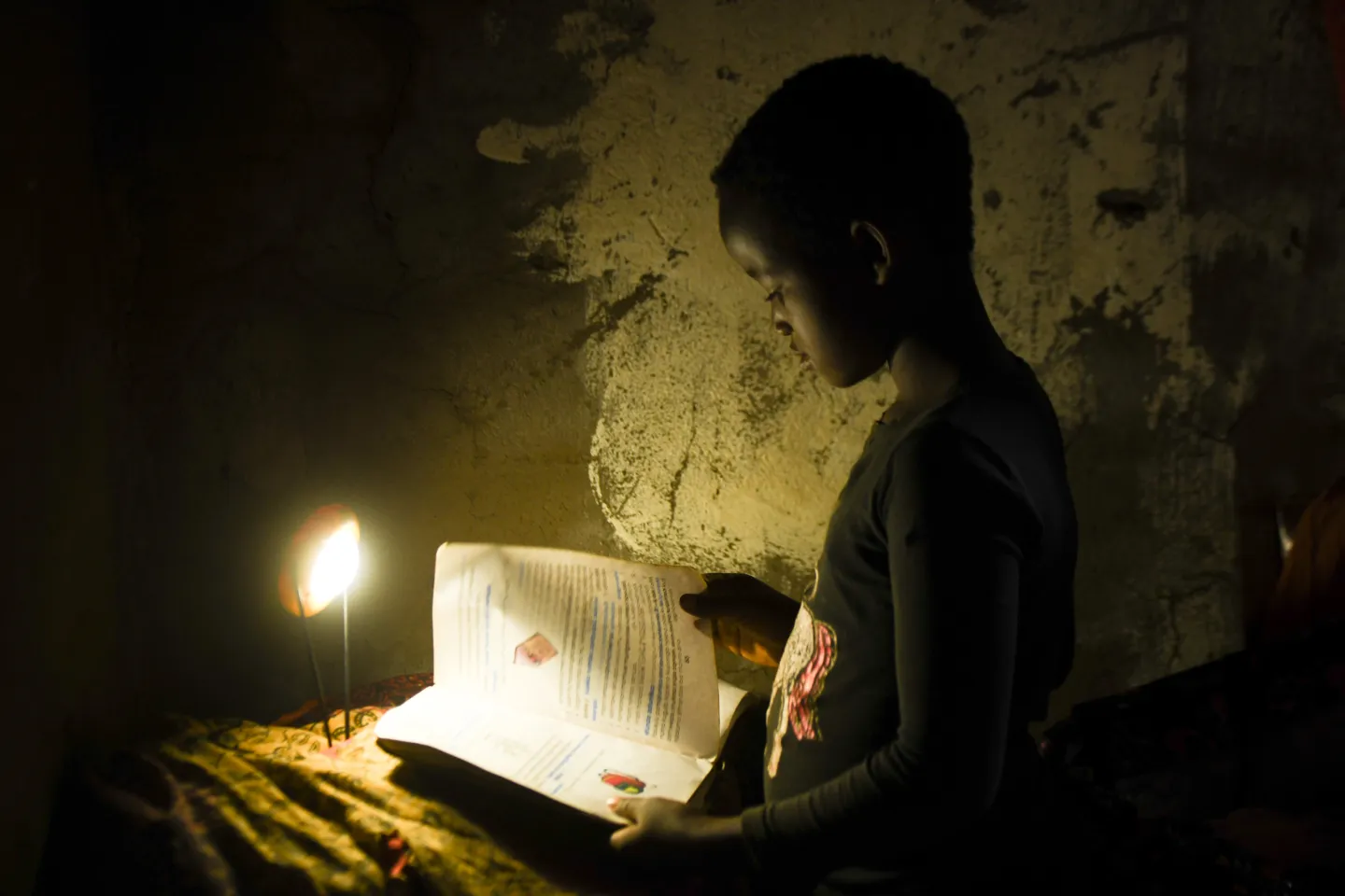 A child doing her school work at home with a candle