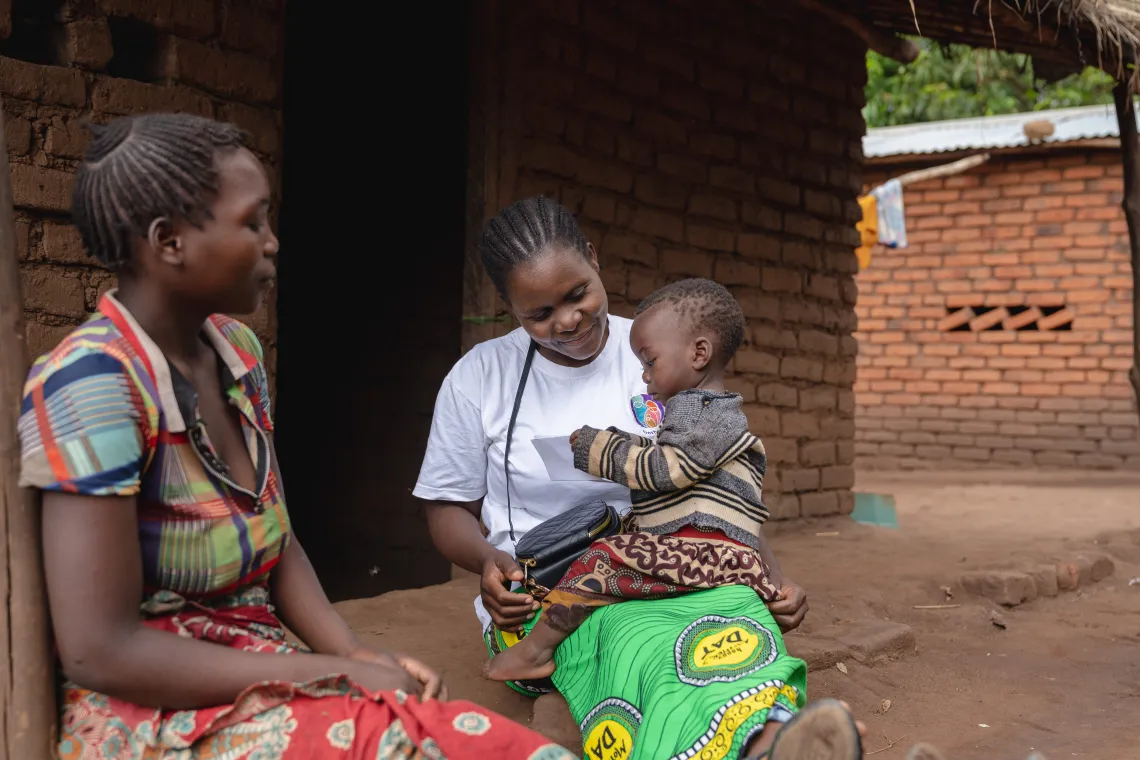 Violet Saulo and her daughter Margaret interact with health worker Gloria Ngulube outside their home 