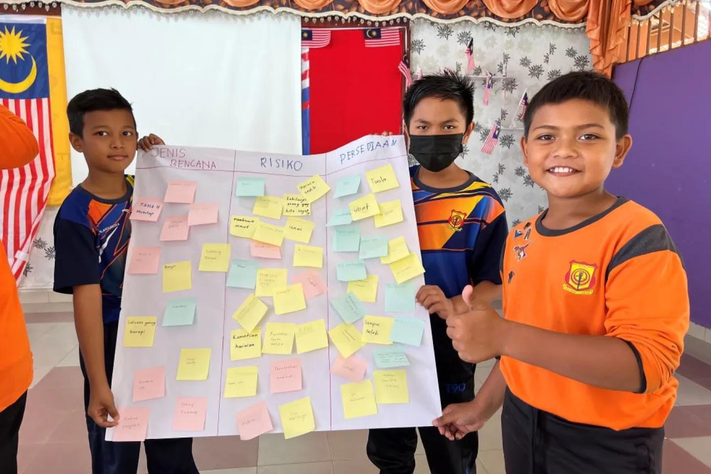 Three children show a poster they created with a disaster mitigation plan