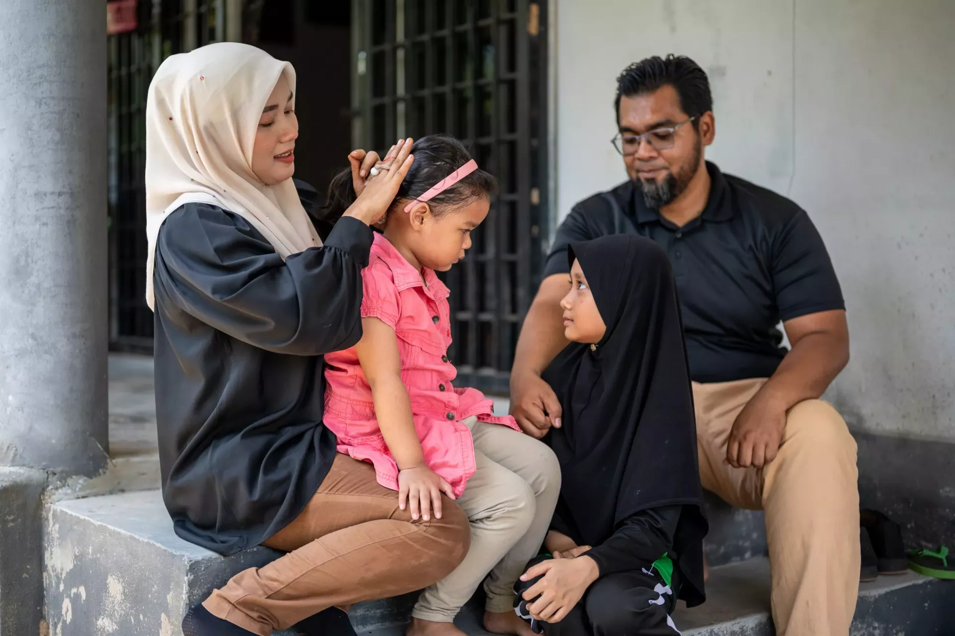 A mother ties her daughter's hair whilst the father looks on