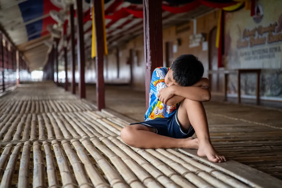 Andrea sits alone on a bamboo floor, resting his head on his folded arms and knees.