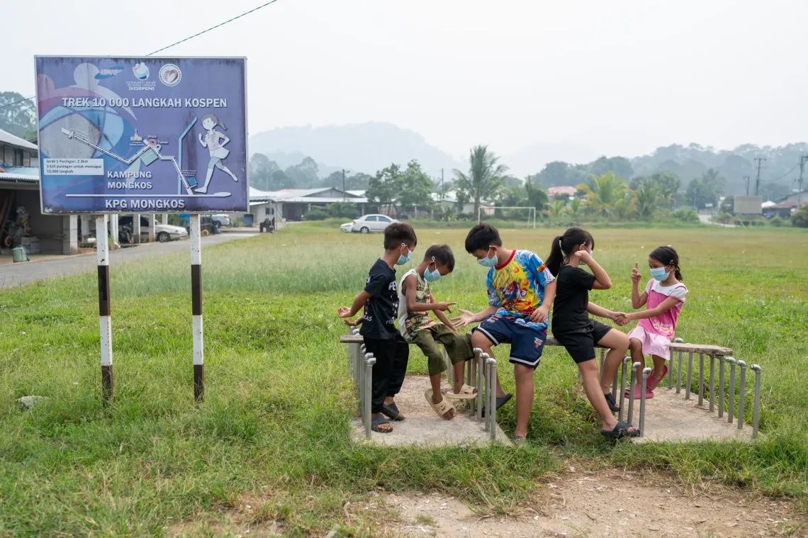 Children wearing face masks spend time outdoors near a field in Serian, as haze hangs over the surrounding landscape.