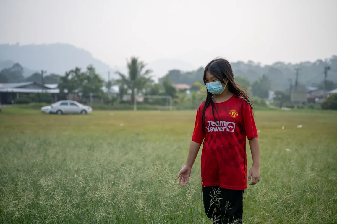 Eva, 12, wearing a face mask, walks through a field in Kampung Mongkos, Serian, Sarawak, during the haze.