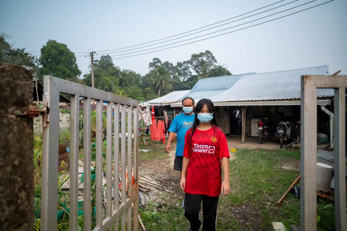 Eva, 12, wearing a face mask, walks outside her home in Kampung Mongkos, Serian, Sarawak, with her uncle behind her.