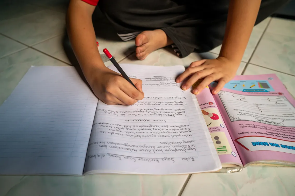 Close-up of Eva&rsquo;s hands as she writes in her notebook while studying at home during a school closure caused by severe haze.