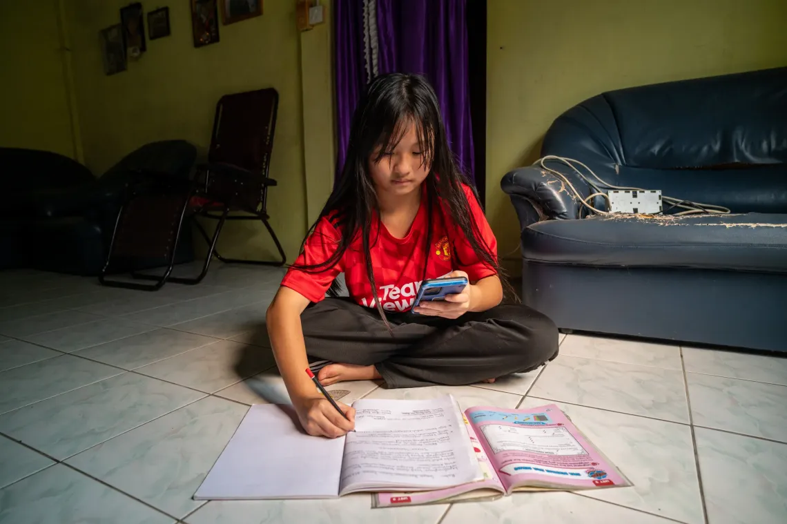 Eva studies at home, using her phone while writing in her workbook during a school closure caused by severe haze.