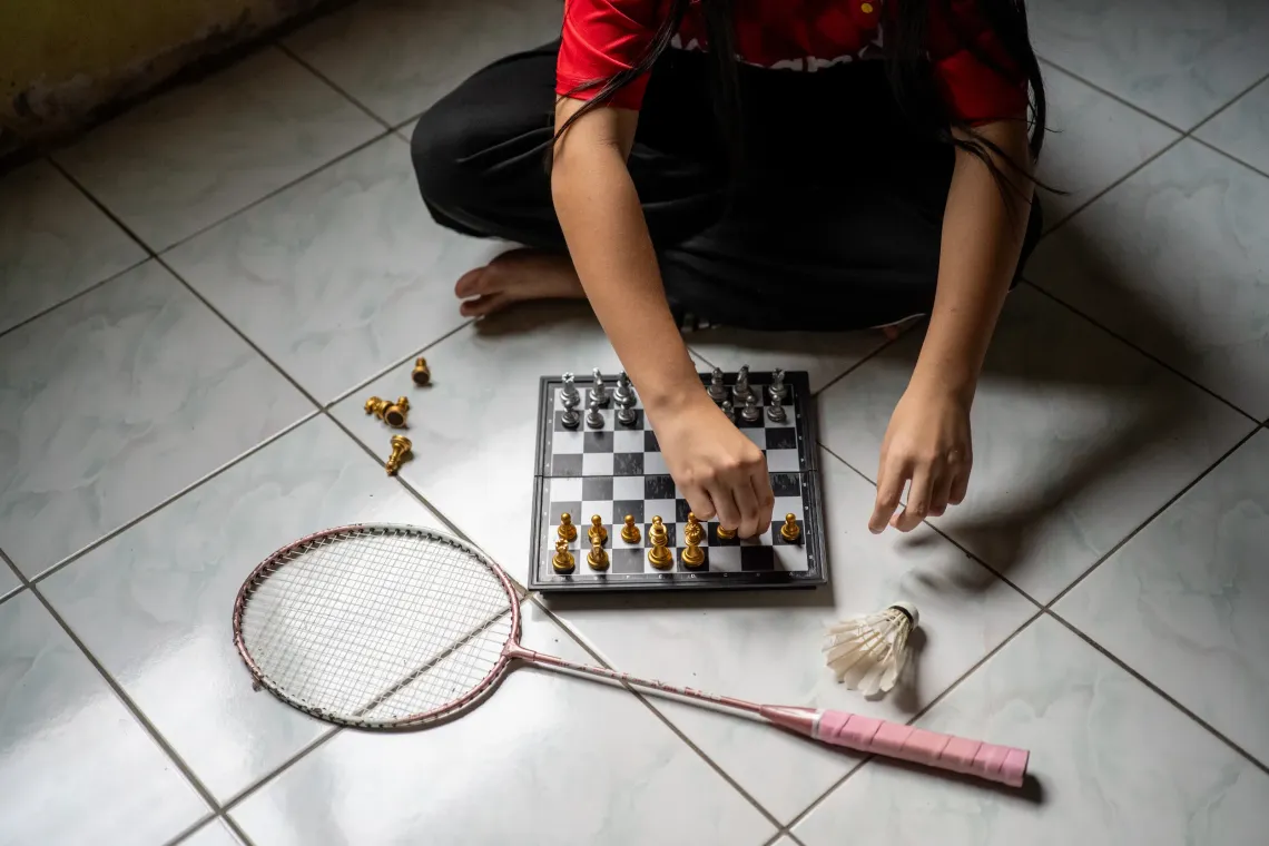 Eva plays chess at home, with a badminton racket and shuttlecock beside her.