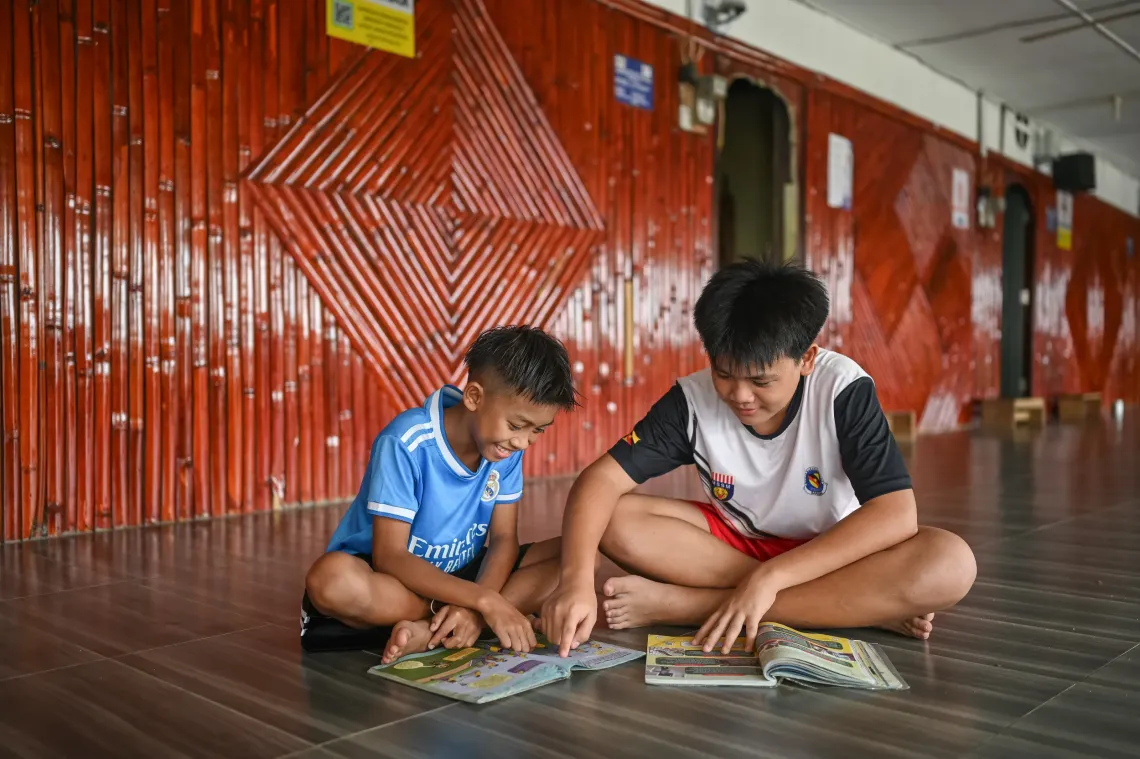 Freddy sits with another child as they read books together on the floor of a longhouse in Serian, Sarawak.